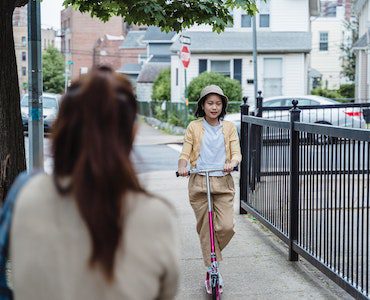 Young adult riding her scooter to meet mom who is waiting at the walkway. What a fun way to have a safe ride home.