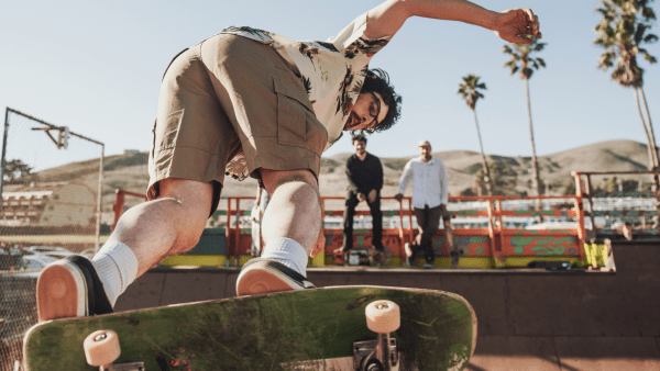 Two men watch as a skateboarder performs a trick with confidence and ease in broad daylight in the park.