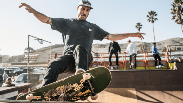 A man performing skateboard tricks with ease and confidence with three other skateboarders on the side.