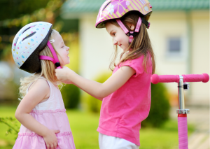 Two kids in pink wear their helmets before their scooter ride. 