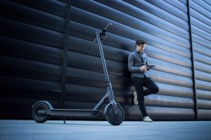 Understanding the overview of an electric scooter and its features is as essential as a person standing beside their electric scooter, holding their phone in front to capture its details. They document the design, specifications, and characteristics, helping them make an informed choice.