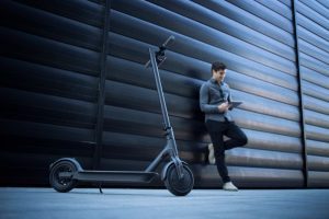 a person standing beside their electric scooter, holding their phone in front to capture electric scooter's best details.