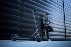 a person standing beside their electric scooter, holding their phone in front to capture its details