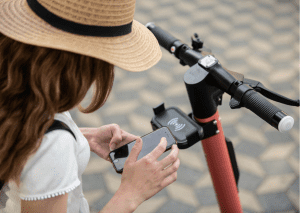 Woman with a scooter and a hat holds her phone while resting.