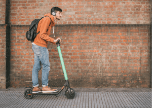 A man with a backpack and brown jacket uses his scooter for traveling. 