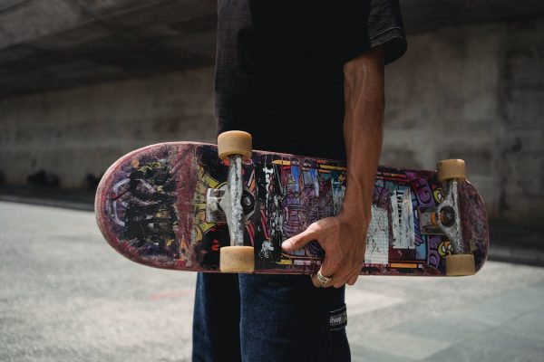 A man wearing black shirt with a ring on his finger is holding his board ready for skateboarding with his friends