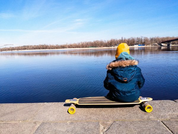 A skater facing the sea while sitting on her skating board with yellow wheels
