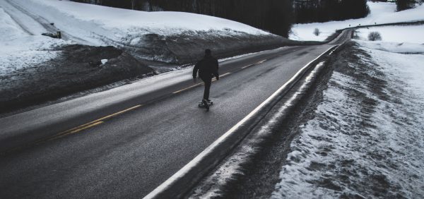 A skateboarder is riding alone on a winterized road with his skating board