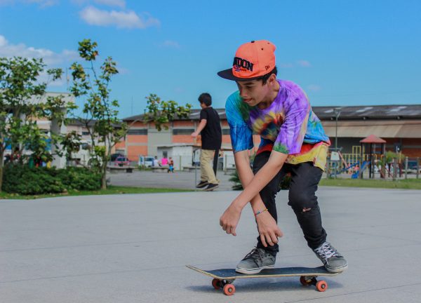 Teenager in a custom tie-dye shirt performing a trick on a custom skateboard at a park.
