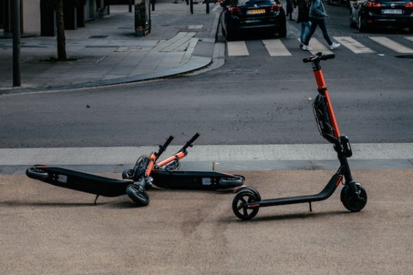 An orange and black scooter with a kickstand is parked conveniently while the two other scooters without kickstands lie on the ground. 