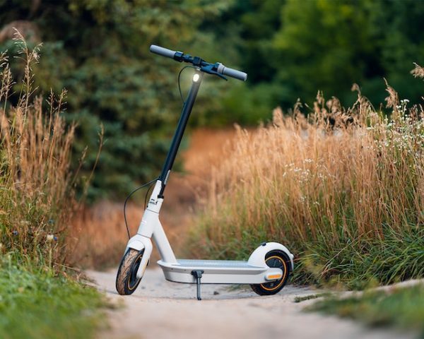 A white and black scooter with a scooter stand is positioned in a hilly area with grassy terrain on the side.