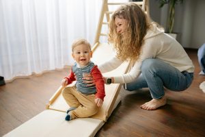 a mother helping her kid on a wooden indoor slide