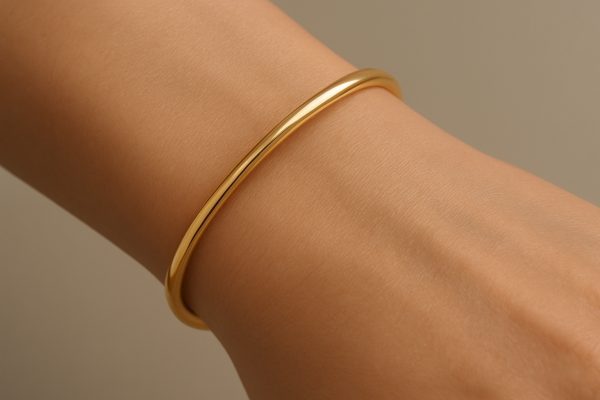 A slender gold cuff bracelet fitted snugly on a wrist, showing smooth contours and comfort.