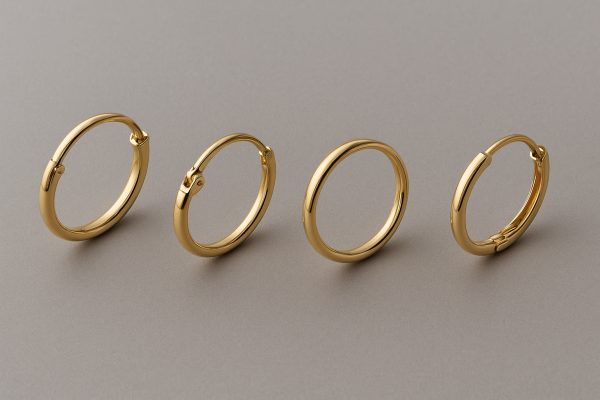 Four gold hoops with different clasps, each clearly displayed on a matte gray pad for design comparison.