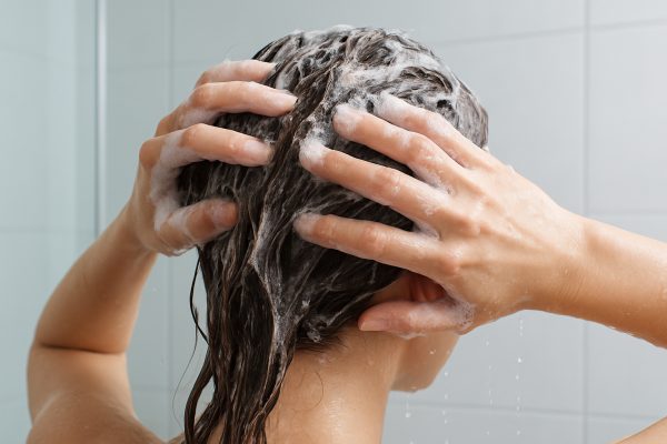 Close-up of shampoo lathering in hair, water droplets rinsing away clay in a modern bathroom.