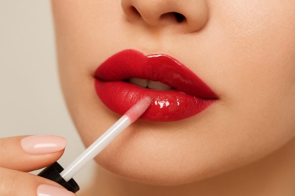 Model applies clear gloss to half-red lips, showing matte vs glossy split.