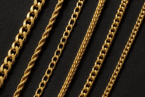 Cuban, rope, Figaro, and wheat gold chains arranged in rows on a charcoal velvet pad, each style distinct.