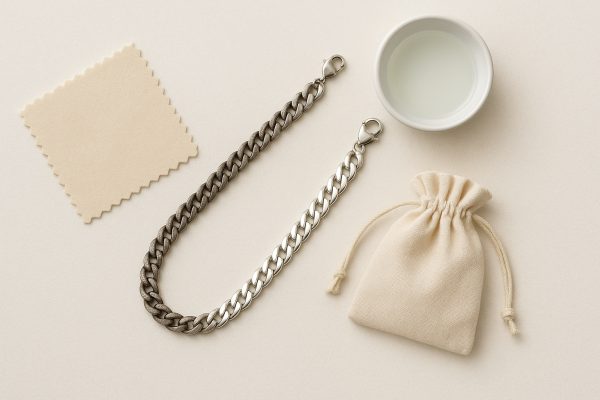 Flat lay of a men's silver chain with cleaning cloth, cleaning solution, and pouch on a pale background.