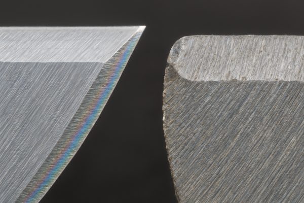 Ultra macro shot of two razor blade edges, one pristine, one slightly worn, showing steel grain and micro-chipping.