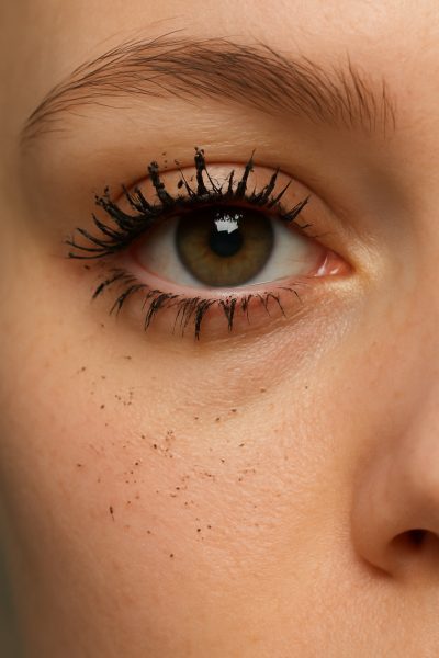 Close-up of eye with clumpy waterproof mascara and flakes under the eye, softly blurred background.
