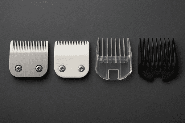 Macro view of clipper blades, guards, and attachments in stainless steel, white ceramic, and clear plastic, arranged linearly for direct material comparison.