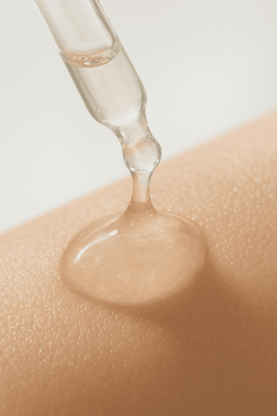 Macro shot of snail mucin serum dropper above hydrated, glowing skin, in a clean, clinical setting.