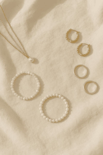 A refined flat lay of gold, silver, and pearl jewelry on ivory linen.