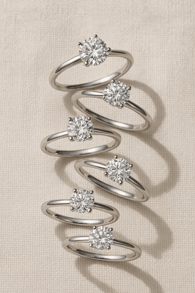 Spiral arrangement of delicate platinum engagement rings with flawless diamonds on a cream linen backdrop.