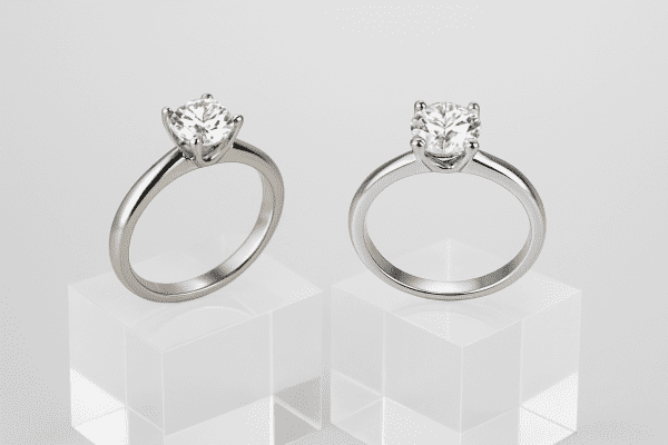 Studio photo of two lab grown diamond solitaire rings, one in white gold, one in silver, on clear pedestals.