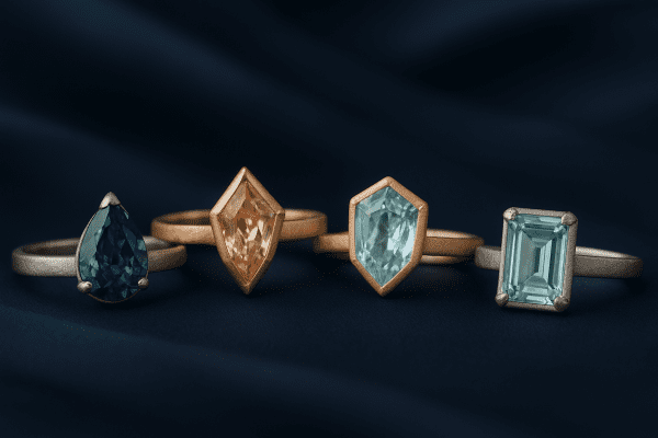 Assorted engagement rings with rare gemstone cuts and mixed metals displayed on navy silk.