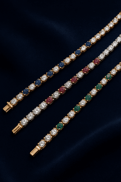 Yellow, white, and rose gold tennis bracelets with diamonds and colored gemstones on navy velvet.