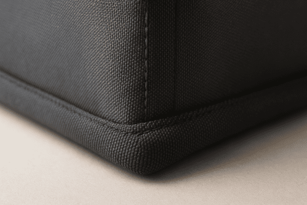 Macro view of cooler bag base, showing reinforced seams, thick fabric, and rugged construction on neutral studio surface.